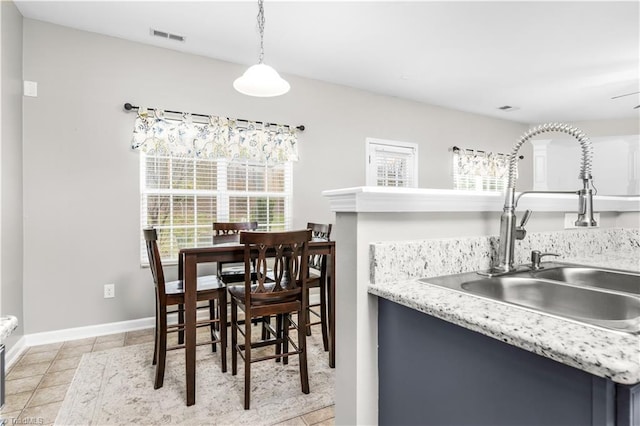 kitchen with light tile patterned floors, baseboards, light countertops, pendant lighting, and a sink