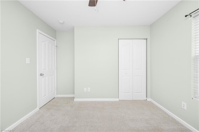 unfurnished bedroom featuring a ceiling fan, a closet, light carpet, and baseboards