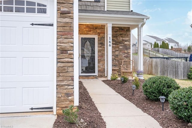 doorway to property with a garage, a shingled roof, stone siding, fence, and a porch