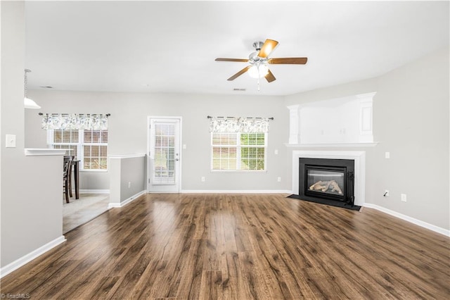 unfurnished living room with dark wood-type flooring, a fireplace with flush hearth, visible vents, a ceiling fan, and baseboards