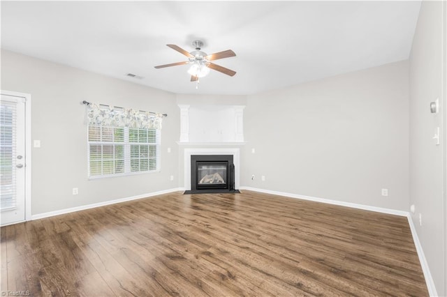 unfurnished living room with a fireplace with flush hearth, wood finished floors, visible vents, and baseboards