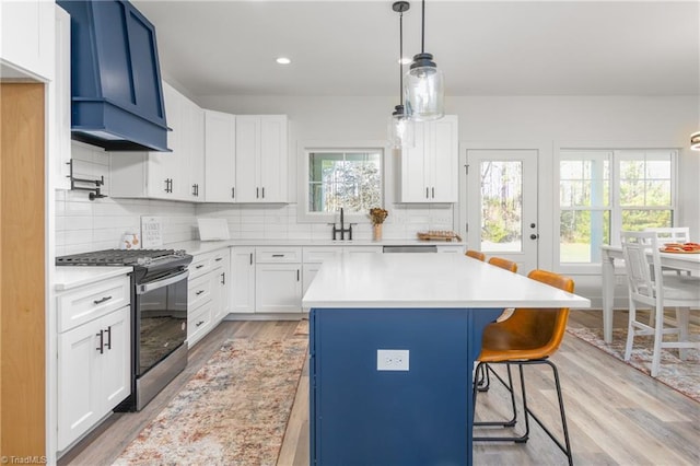 kitchen featuring white cabinets, black gas stove, light hardwood / wood-style floors, plenty of natural light, and a kitchen island