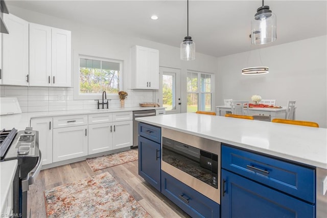 kitchen featuring pendant lighting, light hardwood / wood-style flooring, blue cabinetry, appliances with stainless steel finishes, and white cabinetry