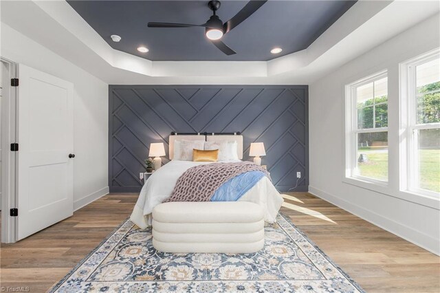 bedroom featuring light hardwood / wood-style floors, a raised ceiling, and ceiling fan