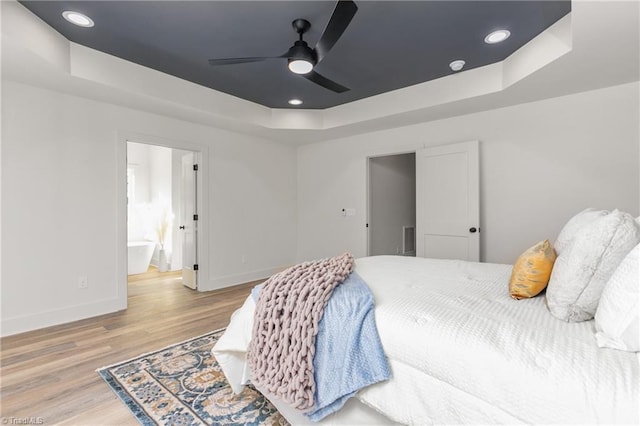 bedroom featuring ensuite bathroom, a raised ceiling, ceiling fan, and hardwood / wood-style flooring