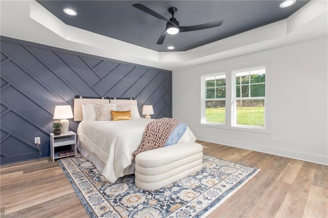 bedroom featuring ceiling fan, light wood-type flooring, and a tray ceiling