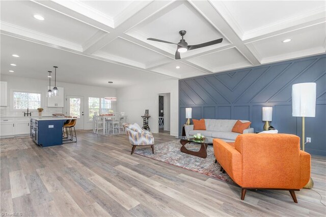 living room featuring coffered ceiling, ceiling fan, beamed ceiling, and light hardwood / wood-style flooring