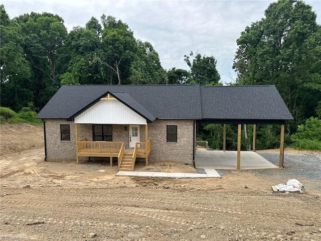 view of front facade featuring brick siding, a carport, a shingled roof, and dirt driveway