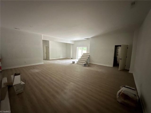 unfurnished living room featuring wood finished floors, baseboards, and stairs