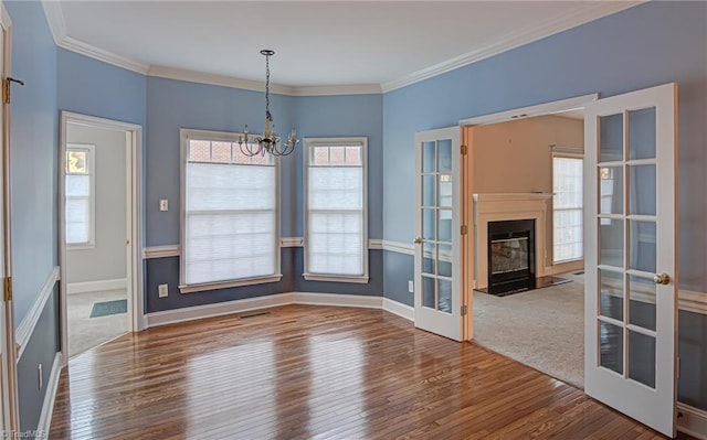 unfurnished dining area with ornamental molding, french doors, wood-type flooring, and a notable chandelier