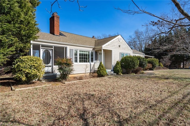 view of front of home with entry steps, a front lawn, a chimney, and a sunroom