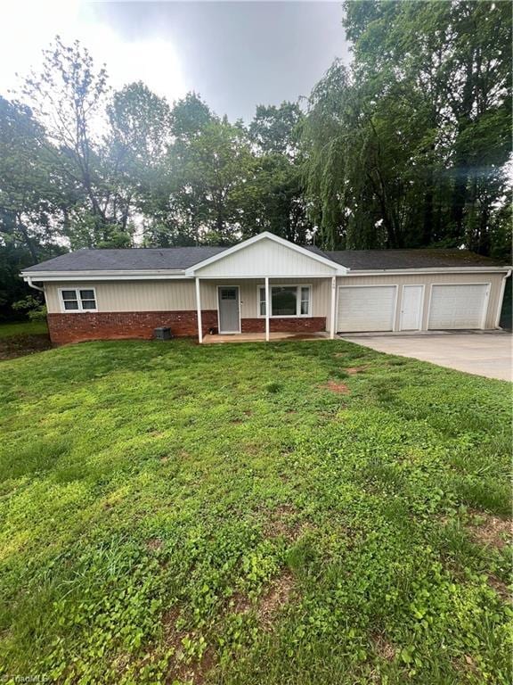 ranch-style house featuring a front yard, covered porch, brick siding, a detached garage, and view of wooded area