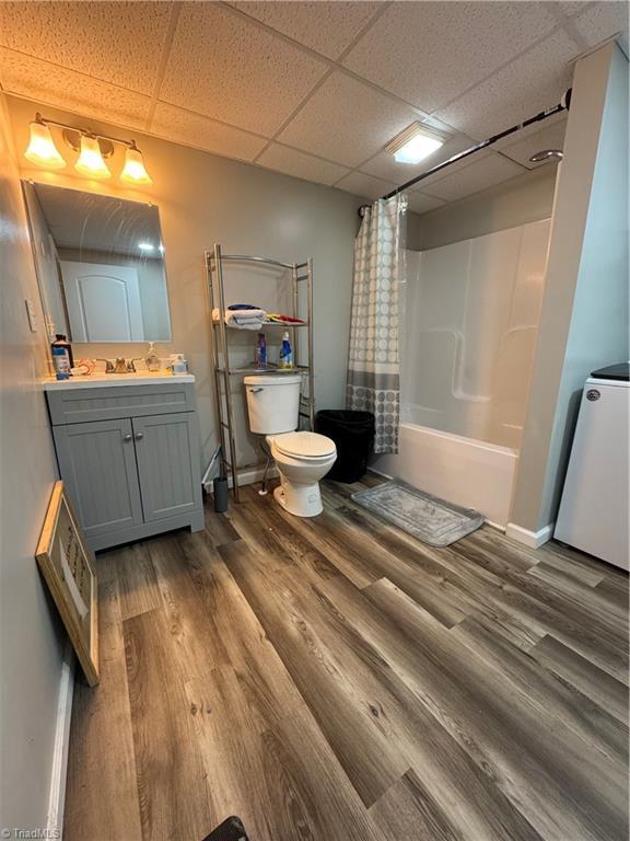 bathroom featuring wood finished floors, shower / tub combo, a paneled ceiling, toilet, and vanity