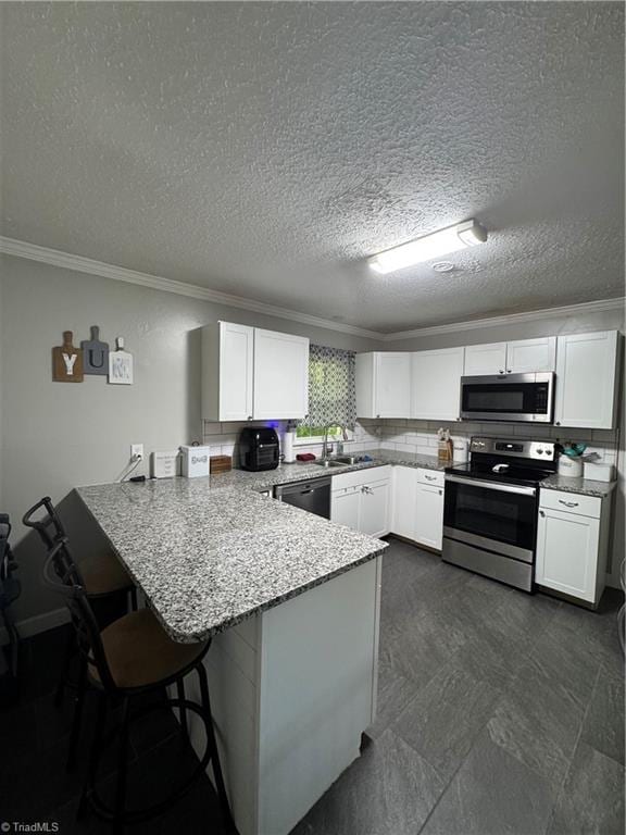 kitchen with appliances with stainless steel finishes, crown molding, a peninsula, white cabinetry, and a sink