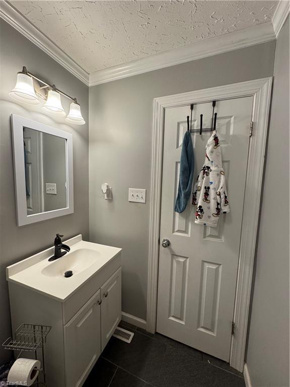 bathroom with vanity, ornamental molding, tile patterned floors, a textured ceiling, and baseboards