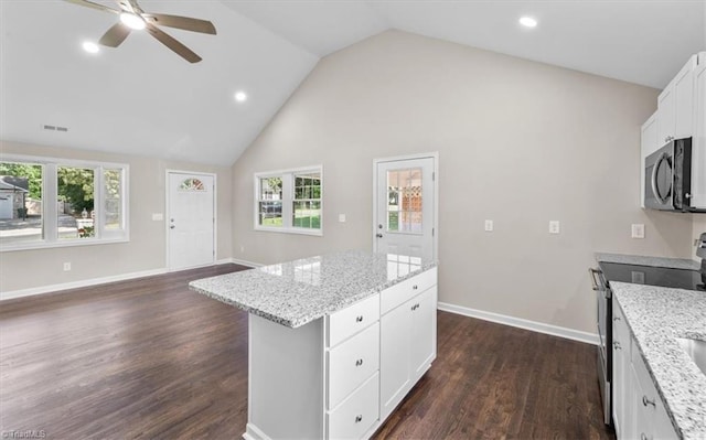 kitchen with dark wood-type flooring, appliances with stainless steel finishes, a center island, light stone countertops, and white cabinets