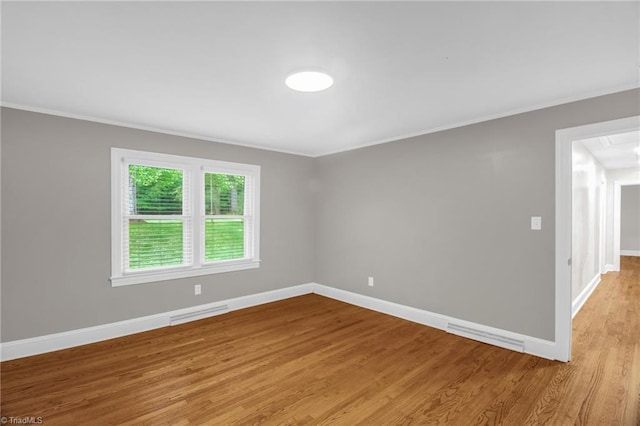 spare room with crown molding, light wood-style floors, and baseboards