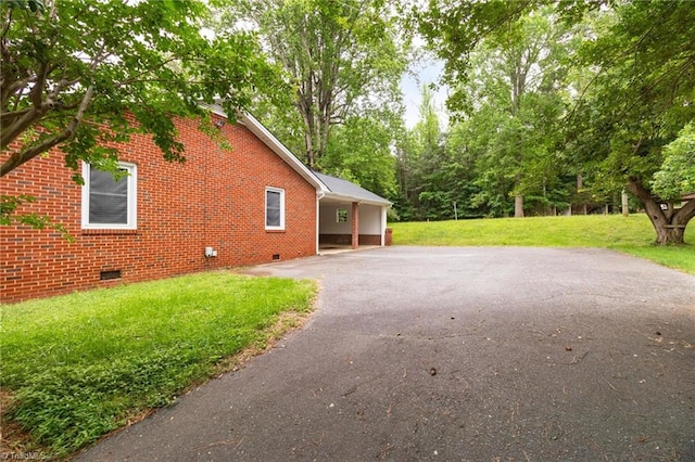 view of side of property featuring crawl space, driveway, a lawn, and brick siding