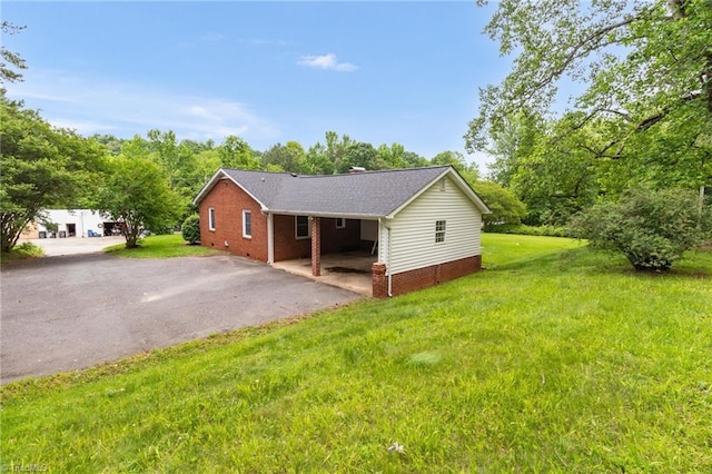 view of side of home featuring asphalt driveway, a yard, and brick siding
