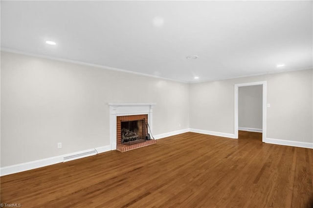 unfurnished living room featuring a brick fireplace, wood finished floors, baseboards, recessed lighting, and crown molding