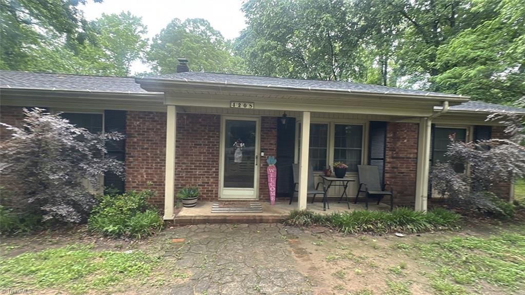view of front of property with covered porch, brick siding, and a chimney