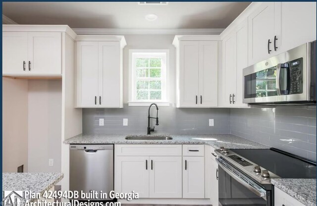 kitchen with appliances with stainless steel finishes, white cabinets, tasteful backsplash, and sink