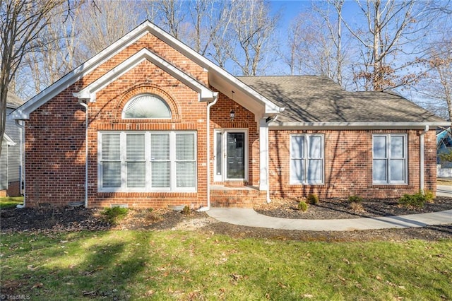 traditional-style house featuring a front lawn, brick siding, and a shingled roof