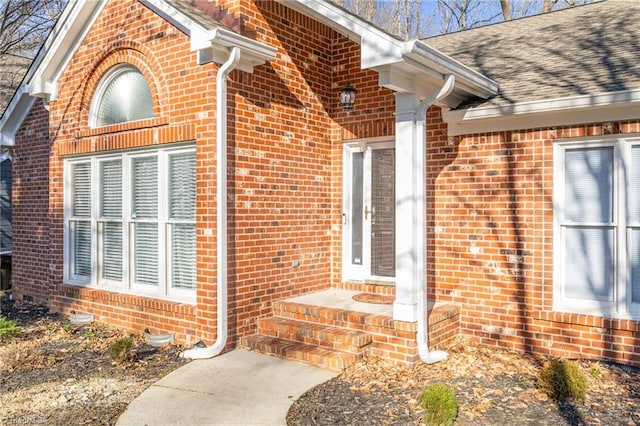 doorway to property with brick siding and roof with shingles