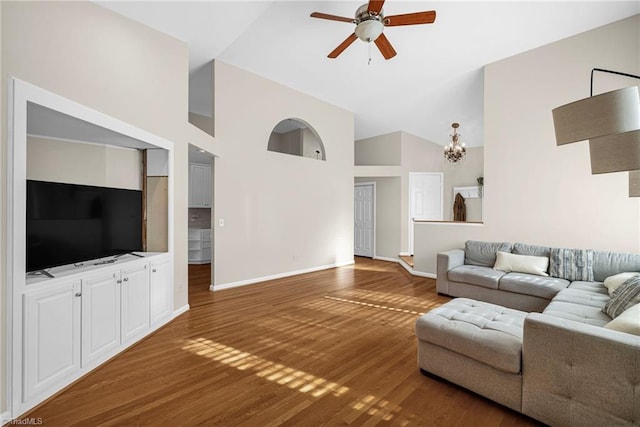 living area featuring ceiling fan with notable chandelier, high vaulted ceiling, baseboards, and wood finished floors