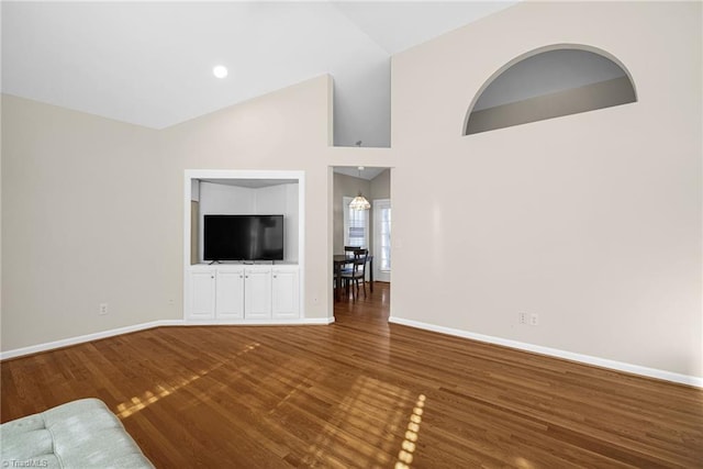 unfurnished living room with high vaulted ceiling, baseboards, and wood finished floors