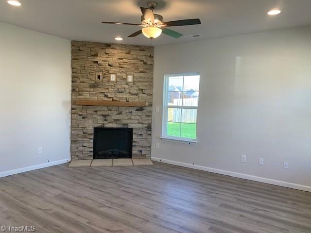 unfurnished living room with light hardwood / wood-style floors, a stone fireplace, and ceiling fan