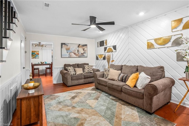 living room with ceiling fan, wooden walls, crown molding, and hardwood / wood-style floors