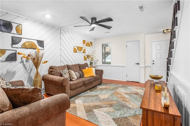 living room with a fireplace, wood walls, a textured ceiling, ceiling fan, and light hardwood / wood-style flooring