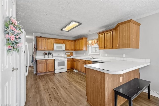 kitchen with sink, decorative light fixtures, kitchen peninsula, white appliances, and light hardwood / wood-style floors