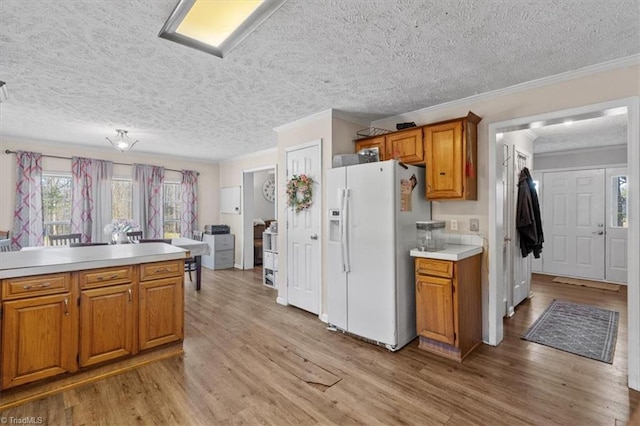 kitchen featuring crown molding, white refrigerator with ice dispenser, light hardwood / wood-style flooring, and a textured ceiling