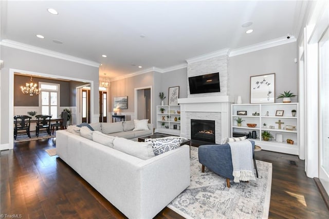 living room with dark wood-type flooring, a notable chandelier, crown molding, and a stone fireplace