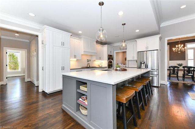 kitchen with a kitchen bar, stainless steel appliances, pendant lighting, a large island with sink, and white cabinets