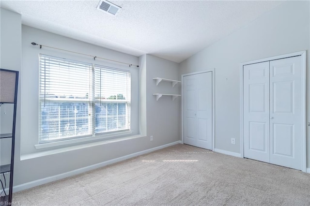 unfurnished bedroom featuring multiple closets, a textured ceiling, light colored carpet, and lofted ceiling