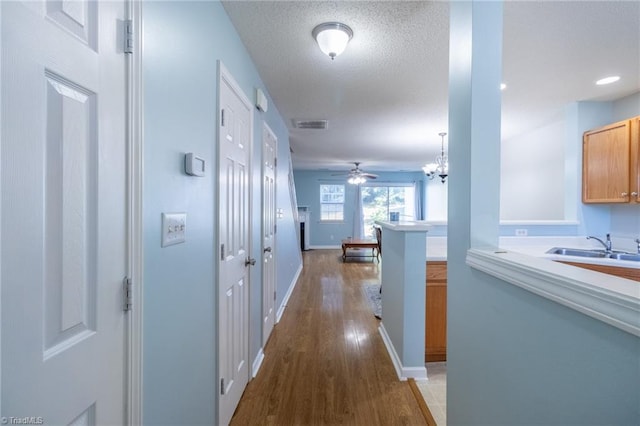 hallway with hardwood / wood-style flooring, a textured ceiling, sink, and an inviting chandelier