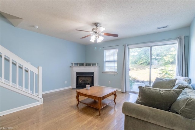 living room with a textured ceiling, light wood-type flooring, and ceiling fan