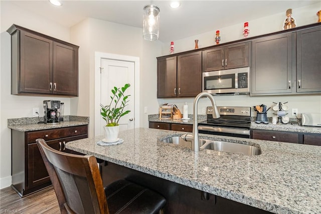 kitchen featuring light stone counters, pendant lighting, dark brown cabinetry, and stainless steel appliances