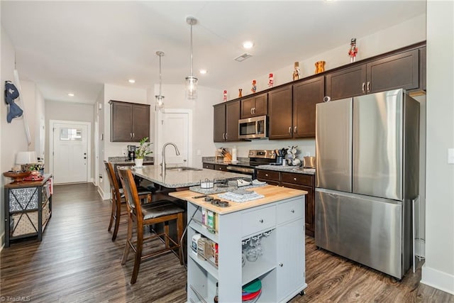 kitchen featuring a center island with sink, stainless steel appliances, light stone counters, dark brown cabinetry, and sink