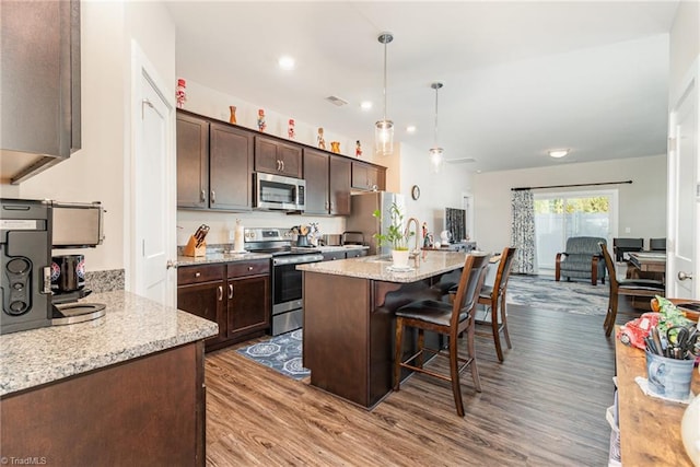 kitchen with hardwood / wood-style floors, a breakfast bar area, stainless steel appliances, hanging light fixtures, and light stone counters