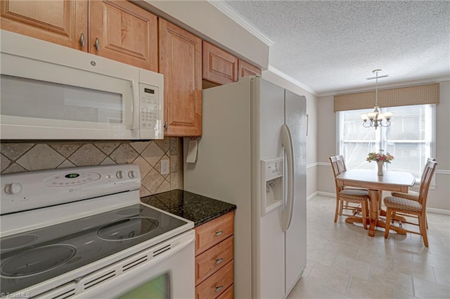 kitchen with hanging light fixtures, a notable chandelier, white appliances, ornamental molding, and dark stone countertops