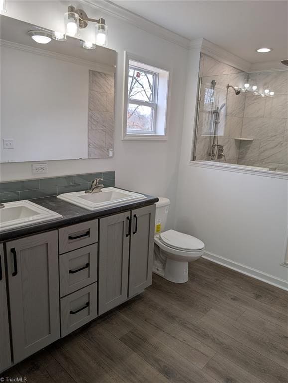 bathroom with tiled shower, toilet, ornamental molding, vanity, and hardwood / wood-style floors