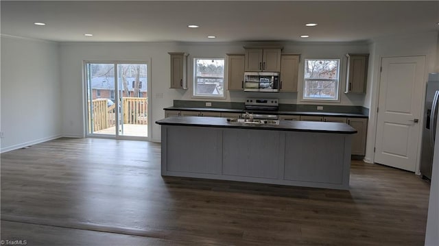 kitchen with dark wood-type flooring, gray cabinets, stainless steel appliances, ornamental molding, and a center island with sink