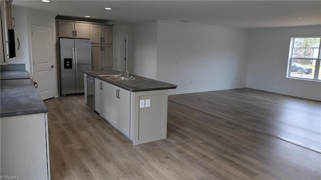 kitchen featuring gray cabinetry, stainless steel appliances, wood-type flooring, ornamental molding, and a center island with sink