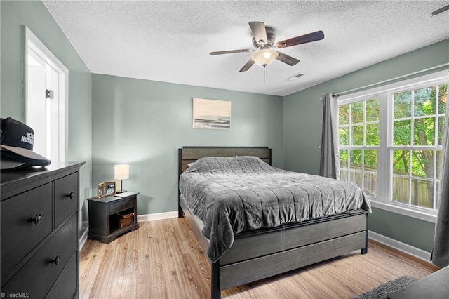 bedroom with baseboards, light wood finished floors, a textured ceiling, and a ceiling fan