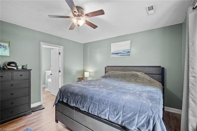 bedroom featuring baseboards, wood finished floors, ensuite bathroom, a textured ceiling, and a ceiling fan