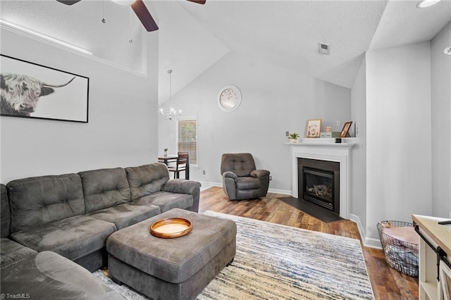 living room with hardwood / wood-style flooring, ceiling fan, vaulted ceiling, a chandelier, and a fireplace with flush hearth